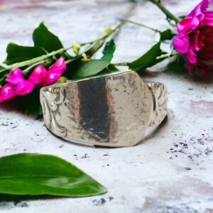 silver ring on a marble slab with green leaves and pink flowers in the background